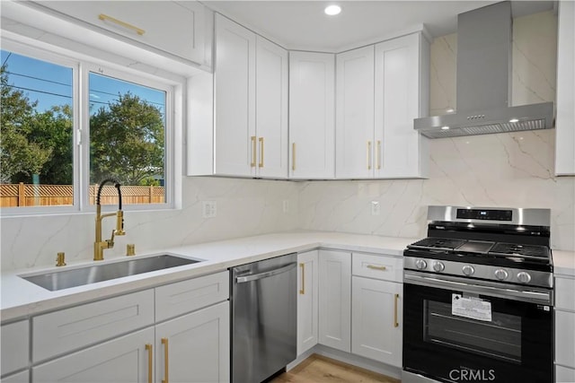 kitchen with appliances with stainless steel finishes, sink, white cabinetry, and wall chimney range hood