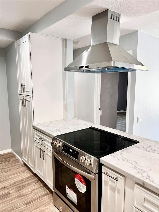 kitchen with white cabinetry, island exhaust hood, light hardwood / wood-style floors, light stone countertops, and stainless steel electric range