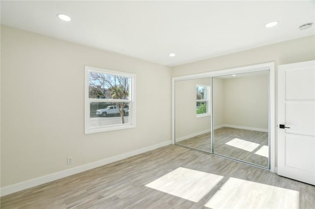 unfurnished bedroom with light hardwood / wood-style floors, multiple windows, and a closet