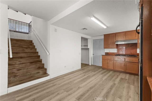 kitchen with stainless steel gas stovetop, light wood-type flooring, and decorative backsplash