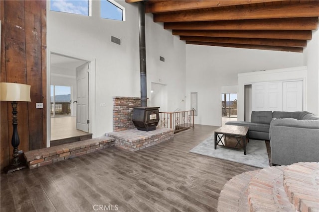 living room featuring a high ceiling, hardwood / wood-style flooring, a wood stove, and beam ceiling