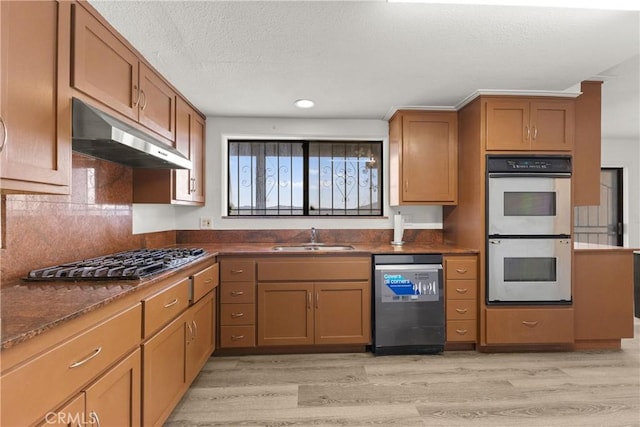 kitchen featuring sink, stainless steel appliances, dark stone countertops, light hardwood / wood-style floors, and a textured ceiling