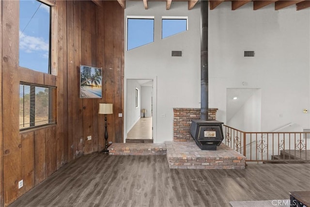 living room featuring a wood stove, wooden walls, a towering ceiling, beamed ceiling, and dark hardwood / wood-style flooring