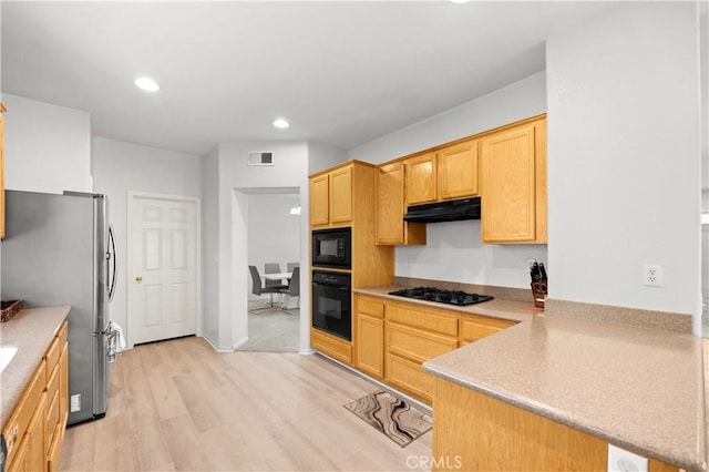 kitchen featuring light brown cabinets, a peninsula, light wood-type flooring, under cabinet range hood, and black appliances