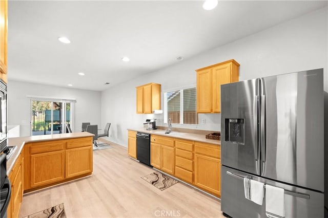 kitchen featuring black dishwasher, stainless steel fridge, light countertops, light wood-type flooring, and a sink