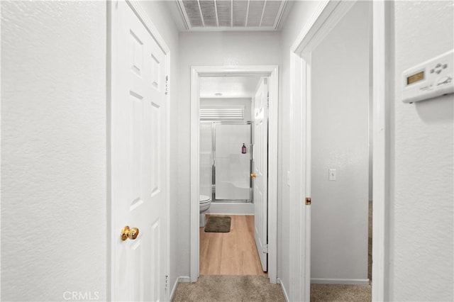 hallway with a textured wall, carpet floors, and visible vents