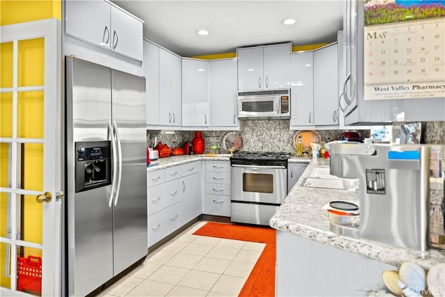 kitchen featuring stainless steel appliances, light tile patterned floors, light stone counters, backsplash, and white cabinets