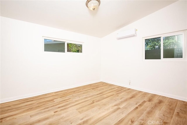 unfurnished room with a wall mounted air conditioner, light hardwood / wood-style flooring, and vaulted ceiling