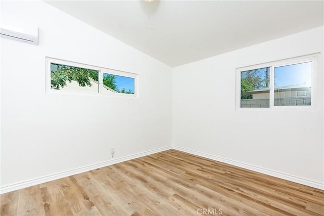 unfurnished room with a wall mounted AC, vaulted ceiling, and light wood-type flooring