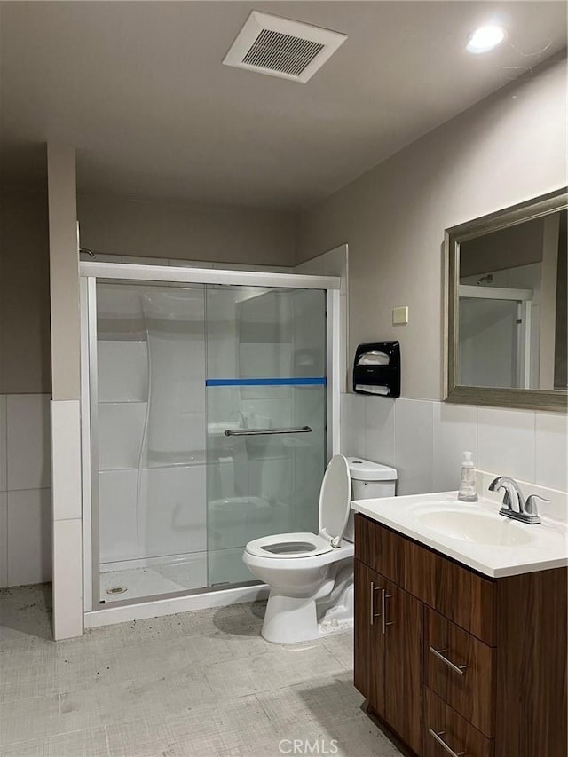 bathroom with vanity, a shower with shower door, tile walls, and toilet