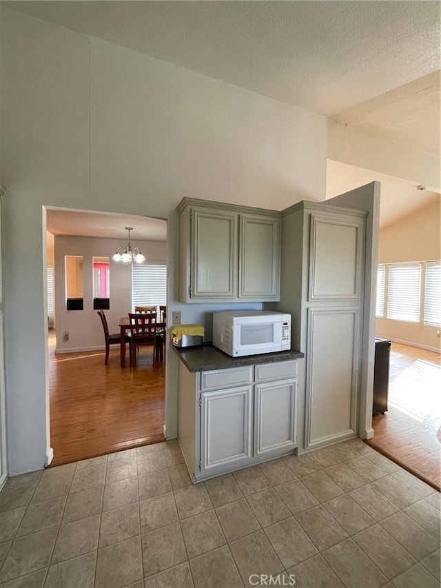 kitchen with a textured ceiling, light tile patterned floors, lofted ceiling, and a notable chandelier