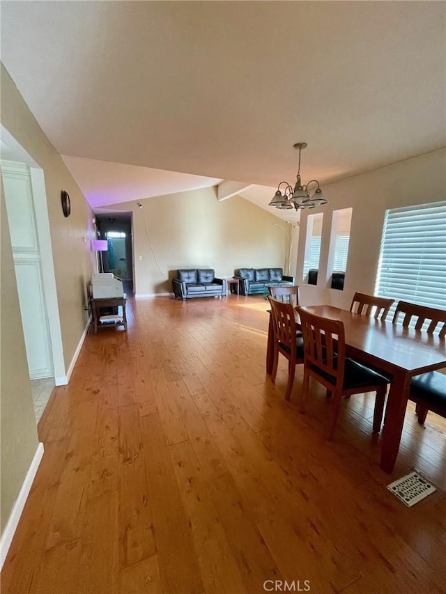 dining area featuring lofted ceiling with beams, hardwood / wood-style flooring, and an inviting chandelier