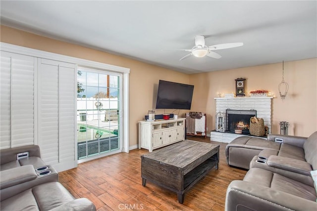 living room with ceiling fan, a brick fireplace, and hardwood / wood-style flooring