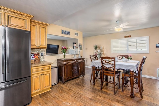 kitchen featuring tasteful backsplash, ceiling fan, stainless steel fridge, hardwood / wood-style flooring, and light stone counters