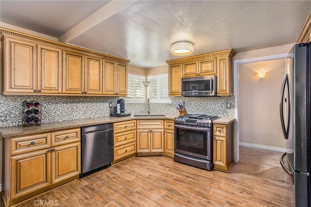 kitchen with appliances with stainless steel finishes, light hardwood / wood-style floors, backsplash, and sink