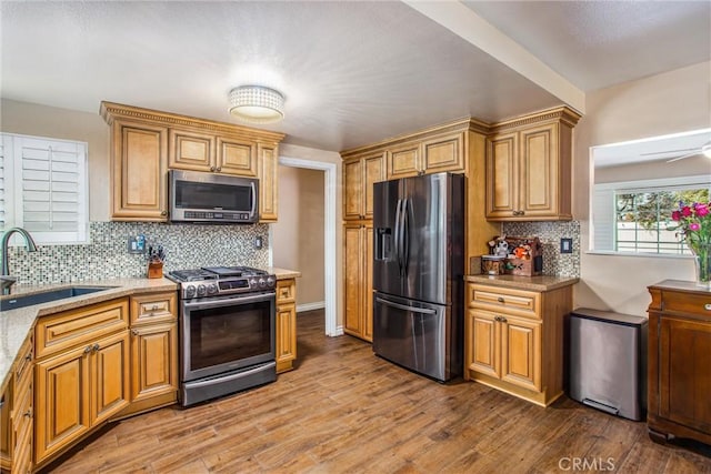 kitchen with tasteful backsplash, hardwood / wood-style floors, sink, light stone countertops, and stainless steel appliances