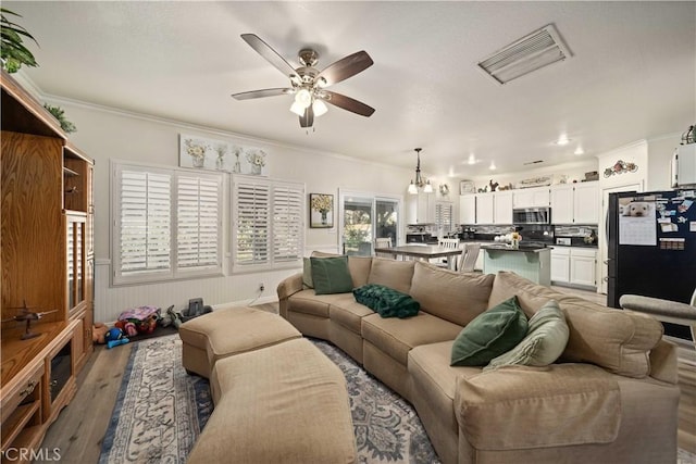 living room featuring crown molding, hardwood / wood-style floors, and ceiling fan with notable chandelier