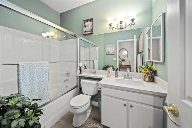 full bathroom featuring vanity, toilet, wood-type flooring, and bath / shower combo with glass door