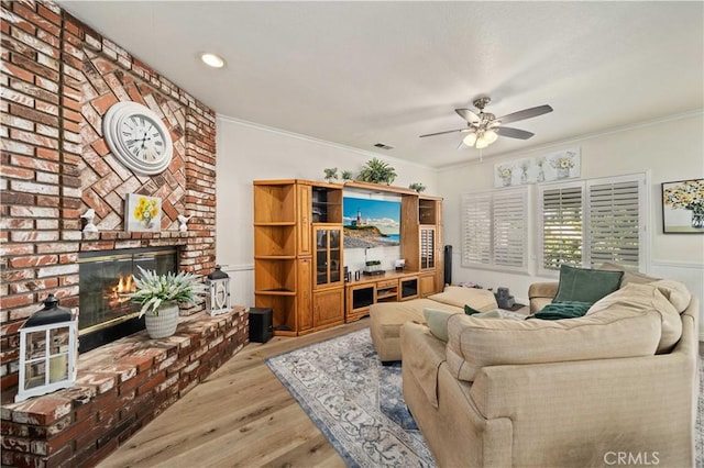 living room featuring light hardwood / wood-style flooring, a brick fireplace, ceiling fan, and crown molding