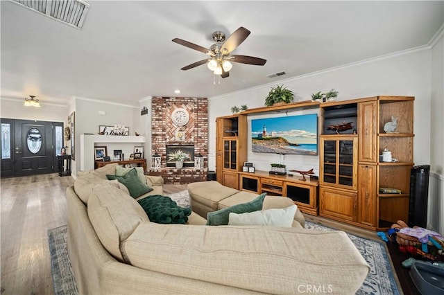 living room featuring a brick fireplace, light hardwood / wood-style flooring, ceiling fan, and crown molding