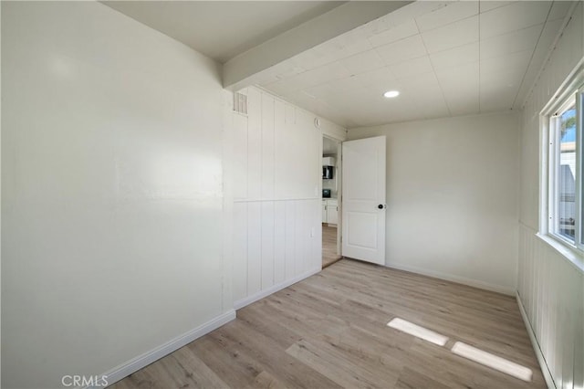 unfurnished room with beam ceiling and light hardwood / wood-style floors