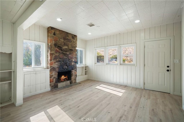 unfurnished living room with a fireplace, light hardwood / wood-style flooring, and wood walls