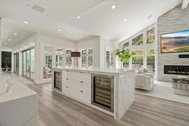 kitchen with a large island, a premium fireplace, light stone counters, white cabinets, and beverage cooler