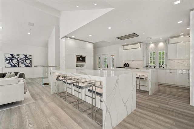 kitchen featuring light hardwood / wood-style flooring, backsplash, a spacious island, white cabinets, and a kitchen bar