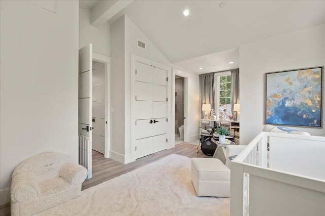 bedroom featuring ensuite bathroom, lofted ceiling with beams, and light wood-type flooring