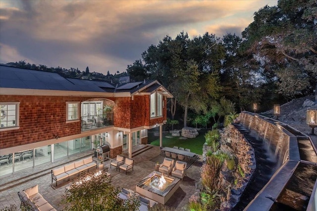 back house at dusk with a balcony, a patio, and an outdoor living space with a fire pit