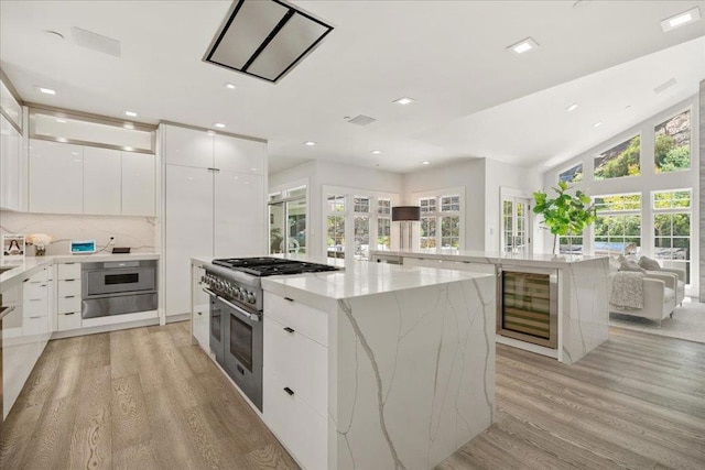 kitchen featuring light stone counters, a kitchen island, light hardwood / wood-style floors, range with two ovens, and white cabinets