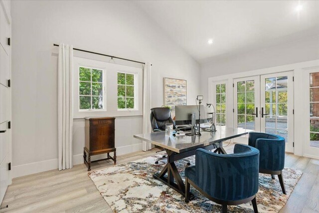 home office with french doors, plenty of natural light, high vaulted ceiling, and light hardwood / wood-style flooring