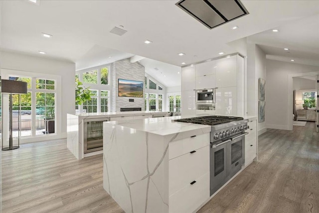 kitchen featuring white cabinetry, light stone countertops, light hardwood / wood-style floors, a kitchen island, and range with two ovens