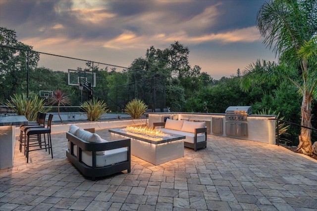 patio terrace at dusk with area for grilling, exterior kitchen, an outdoor bar, and an outdoor living space with a fire pit