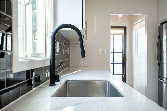 kitchen with light stone countertops, tasteful backsplash, stainless steel refrigerator, and sink