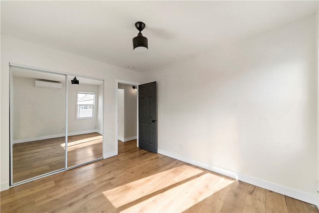 unfurnished bedroom featuring a wall unit AC, ceiling fan, a closet, and hardwood / wood-style floors