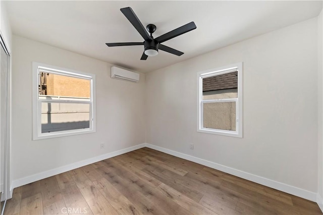 empty room with a wall mounted AC, ceiling fan, and light hardwood / wood-style flooring