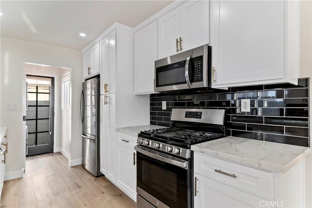 kitchen featuring appliances with stainless steel finishes, backsplash, light stone counters, light hardwood / wood-style flooring, and white cabinetry