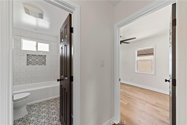 bathroom featuring hardwood / wood-style flooring, ceiling fan, toilet, and tiled shower / bath combo