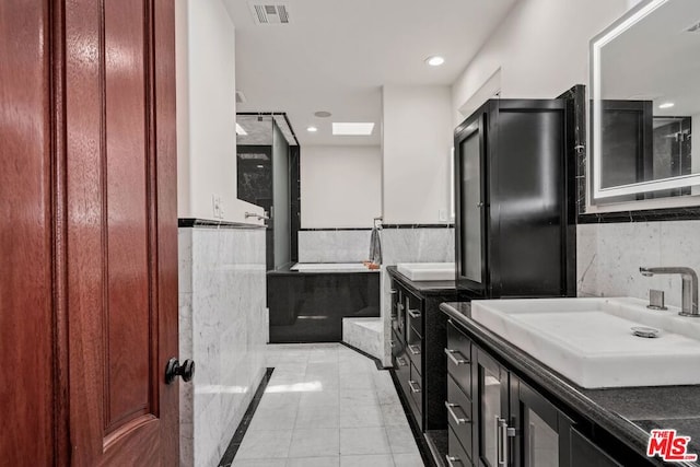 bathroom with a skylight, a bathing tub, vanity, and tile walls