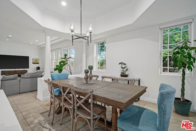 tiled dining space featuring an inviting chandelier, a raised ceiling, decorative columns, and crown molding