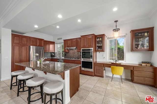 kitchen with dark stone counters, stainless steel appliances, crown molding, a center island with sink, and hanging light fixtures