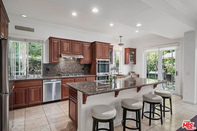 kitchen with sink, light tile patterned floors, an island with sink, decorative light fixtures, and stainless steel appliances