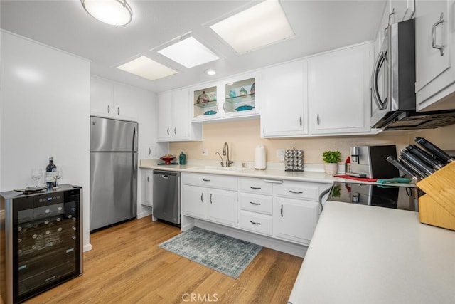 kitchen with light wood-type flooring, stainless steel appliances, beverage cooler, sink, and white cabinetry