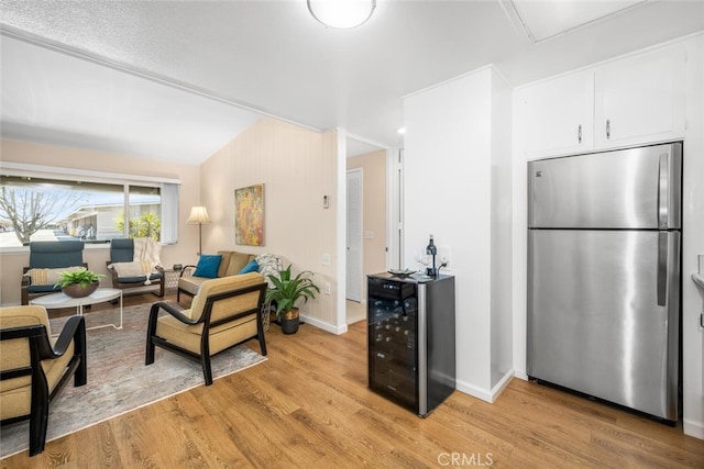 kitchen with light wood-type flooring, vaulted ceiling, beverage cooler, white cabinetry, and stainless steel refrigerator