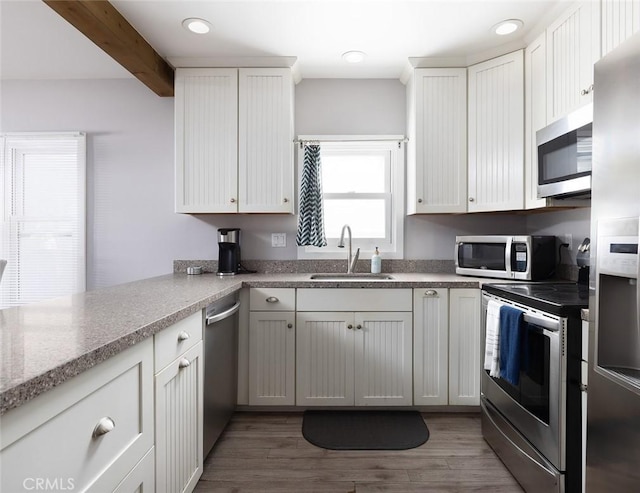 kitchen with sink, stainless steel appliances, beamed ceiling, hardwood / wood-style floors, and white cabinets