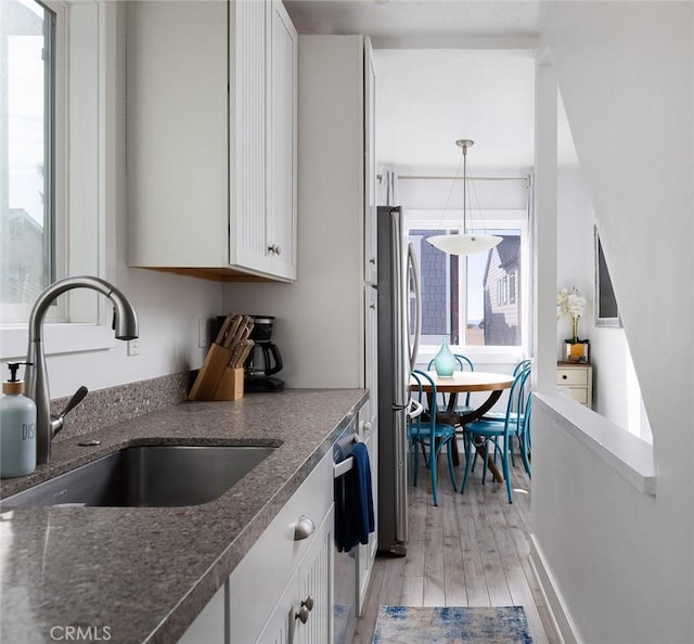 kitchen with white cabinetry, sink, light hardwood / wood-style flooring, stainless steel fridge, and pendant lighting