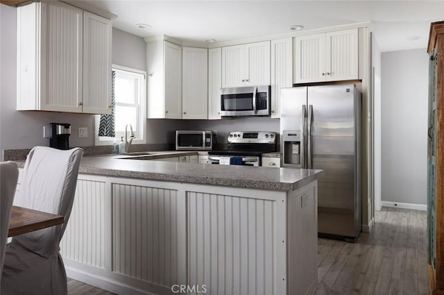 kitchen with kitchen peninsula, sink, white cabinets, and stainless steel appliances