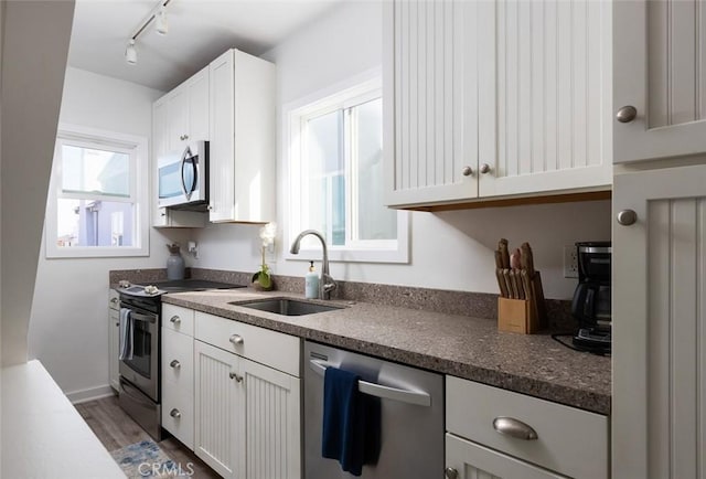 kitchen with sink, rail lighting, hardwood / wood-style flooring, white cabinetry, and stainless steel appliances