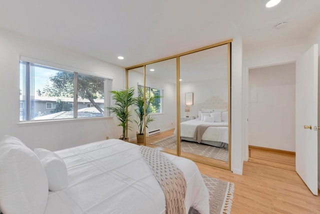 bedroom with hardwood / wood-style flooring, a baseboard heating unit, and a closet